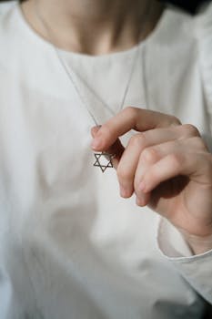 A hand gently holds a Star of David necklace, symbolizing Jewish faith and tradition.